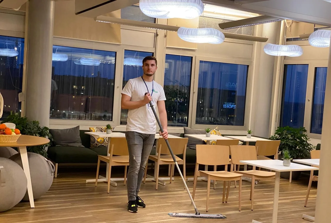 ELLCU:n työvaatteisiin pukeutunut siivooja toimiston oleskelutilassa